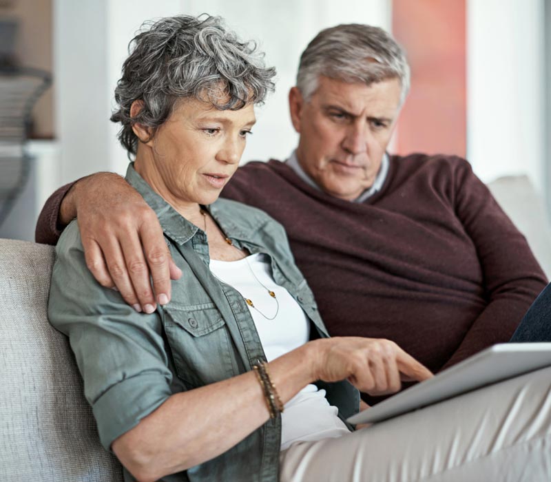 Älteres Paar sitzt auf Couch und sieht auf Tablet